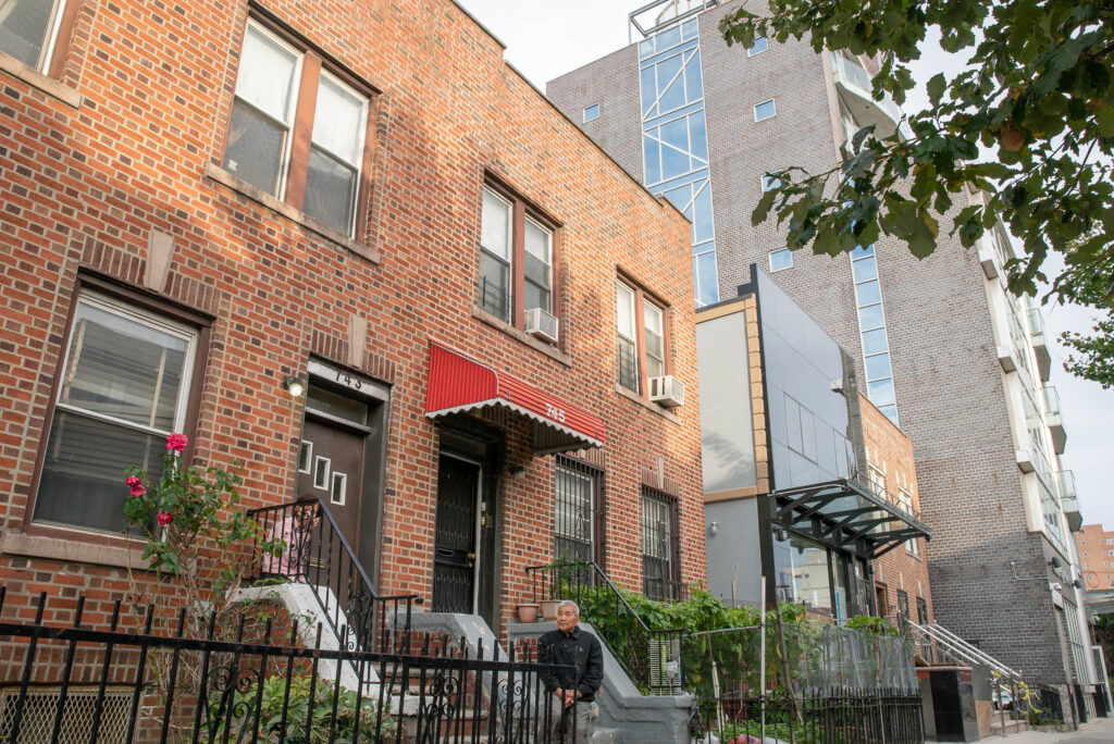 Betty Yu Mom and Dad in front of our house, with new condos on our block From the (Dis)Placed in Sunset Park series Digital C-Type print 17” x 23” 2019